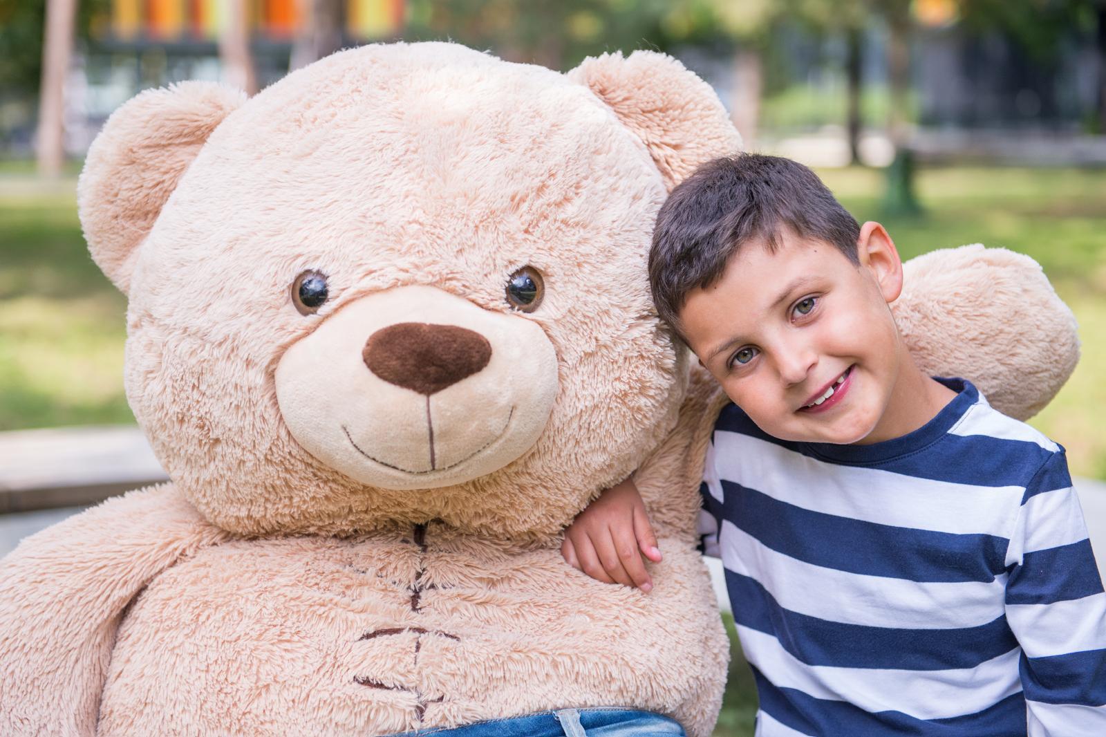 Ein Herzkind lehnt lächelnd an einem überdimensionalen Teddybären — Bild eines glücklichen Moments aus der Begleitung der Elterninitiative